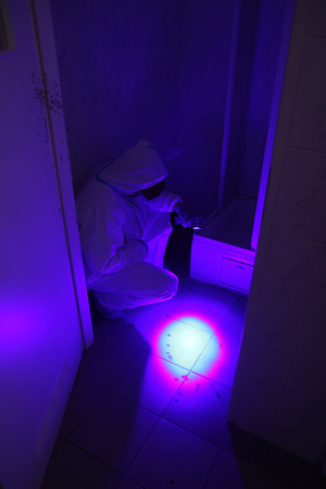 technik w kombinezonie ochronnym oświetla lampą UV plamy na podłodze