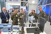 Zdjęcie przedstawia uczestników oglądających laserowy zestaw oględziny, który służy do wyznaczania toru lotu pocisku, określenia kąta jego upadku oraz wskazania miejsca oddania strzału.