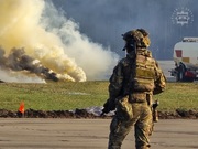 Stojący funkcjonariusz Wydziału Konterrorystycznego podczas ćwiczeń a w oddali widać palącą się świecę dymną