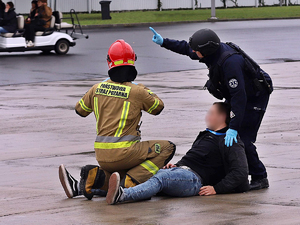 Policjant Oddziałów Prewencji Policji oraz Strażak udzielają pomocy osobie poszkodowanej podczas ćwiczeń na płycie lotniska