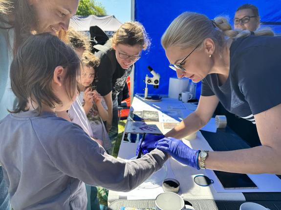Pracownicy Daktyloskopii Centralnego Laboratorium Kryminalistycznego Policji podczas pikniku pokazują młodym osobom swoją pracę dotyczącą odcisków palców.