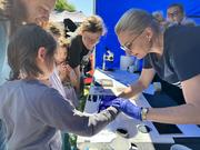 Pracownicy Daktyloskopii Centralnego Laboratorium Kryminalistycznego Policji podczas pikniku pokazują młodym osobom swoją pracę dotyczącą odcisków palców.