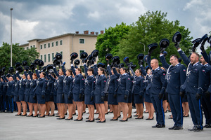Nowi oficerowie Policji stoją jeden obok drugiego w szeregach na placu apelowym Akademii Policji w Szczytnie i unoszą czapki do góry w geście mianowania na pierwszy stopień oficerski.