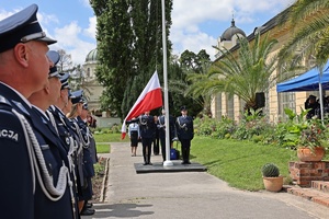 Zdjęcie przedstawia stojących funkcjonariuszy policji stojących w szyku patrzących na poczet flagowy, który podnośni flagę na maszt podczas obchodów Święta Policji centralnego Laboratorium Kryminalistycznego Policji.