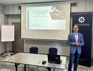 Maciej Świątek podczas wykładu dot. Sympozjum Biegłych Mechanoskopii, zorganizowane przez Wydział Badań Broni, Mechanoskopii i Wypadków Drogowych Centralnego Laboratorium Kryminalistycznego Policji. W tle widać wyświetlony slajd.