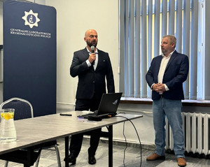 Biegli Centralnego Laboratorium Kryminalistycznego Policji podczas wykładu dot. Sympozjum Biegłych Mechanoskopii, zorganizowane przez Wydział Badań Broni, Mechanoskopii i Wypadków Drogowych Centralnego Laboratorium Kryminalistycznego Policji. W tle widać wyświetlony slajd.